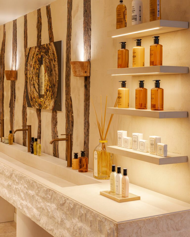Intérieur de la boutique L'Occitane du Marais : vasque en pierre, étagères éclairées et flacons ambrés devant un mur en bois · vrai studio
