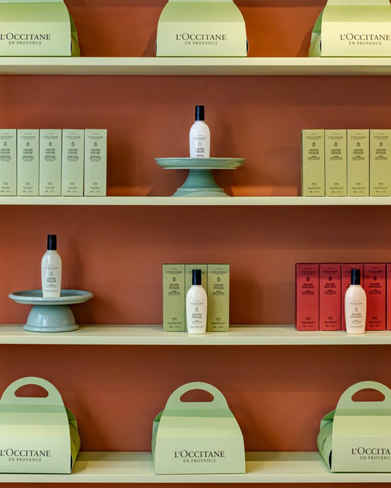 Étagères vert amande de la boutique L'Occitane du Marais, coffrets et flacons sur un mur terracotta · vrai studio