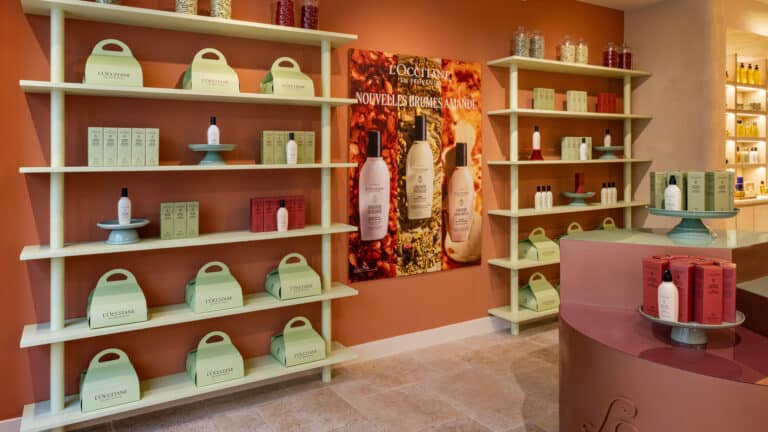 Intérieur de la boutique L'Occitane du Marais : étagères vert amande, affiches Amande et comptoir rond terracotta · vrai studio