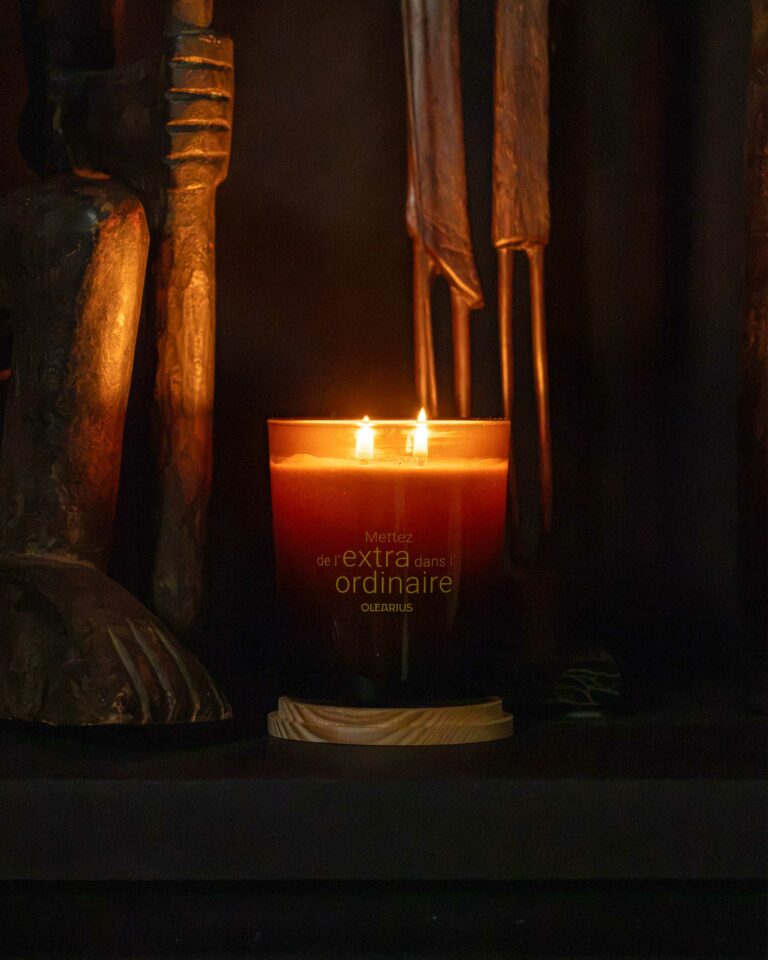 An Olearius Heritage candle lit at the foot of wooden sculptures, creating a chiaroscuro atmosphere — Olearius lifestyle photography · vrai studio