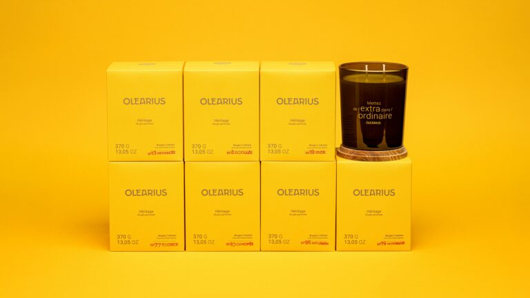 Product shot of the complete line of seven Olearius Heritage candles, gift sets, and a candle removed from its box against a yellow background — Olearius packaging photography · vrai studio