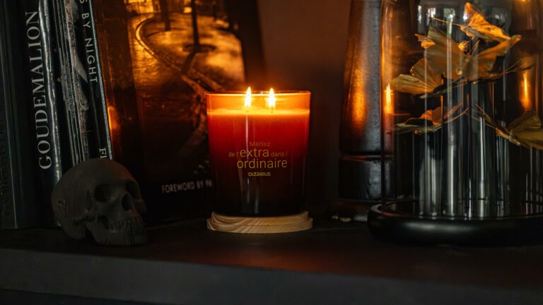 A Heritage candle lit on a shelf among books, a decorative skull, and dried flowers — lifestyle photography by Olearius · vrai studio