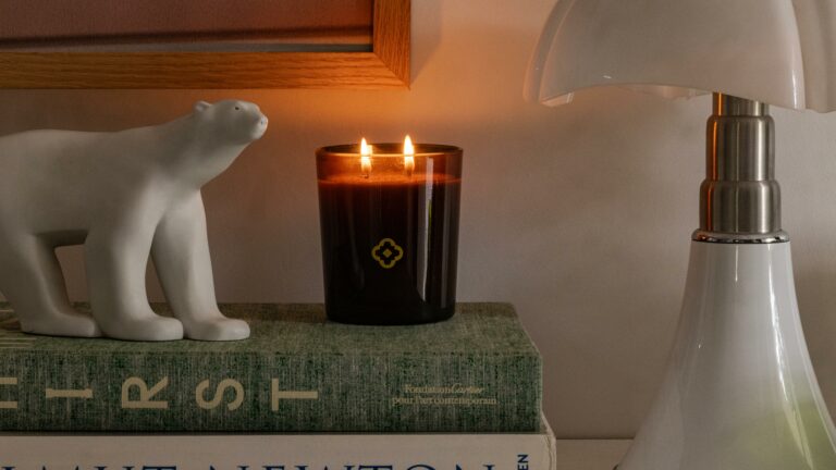 A lit Heritage candle resting on an art book, between a polar bear figurine and a lamp — lifestyle photography by Olearius · vrai studio